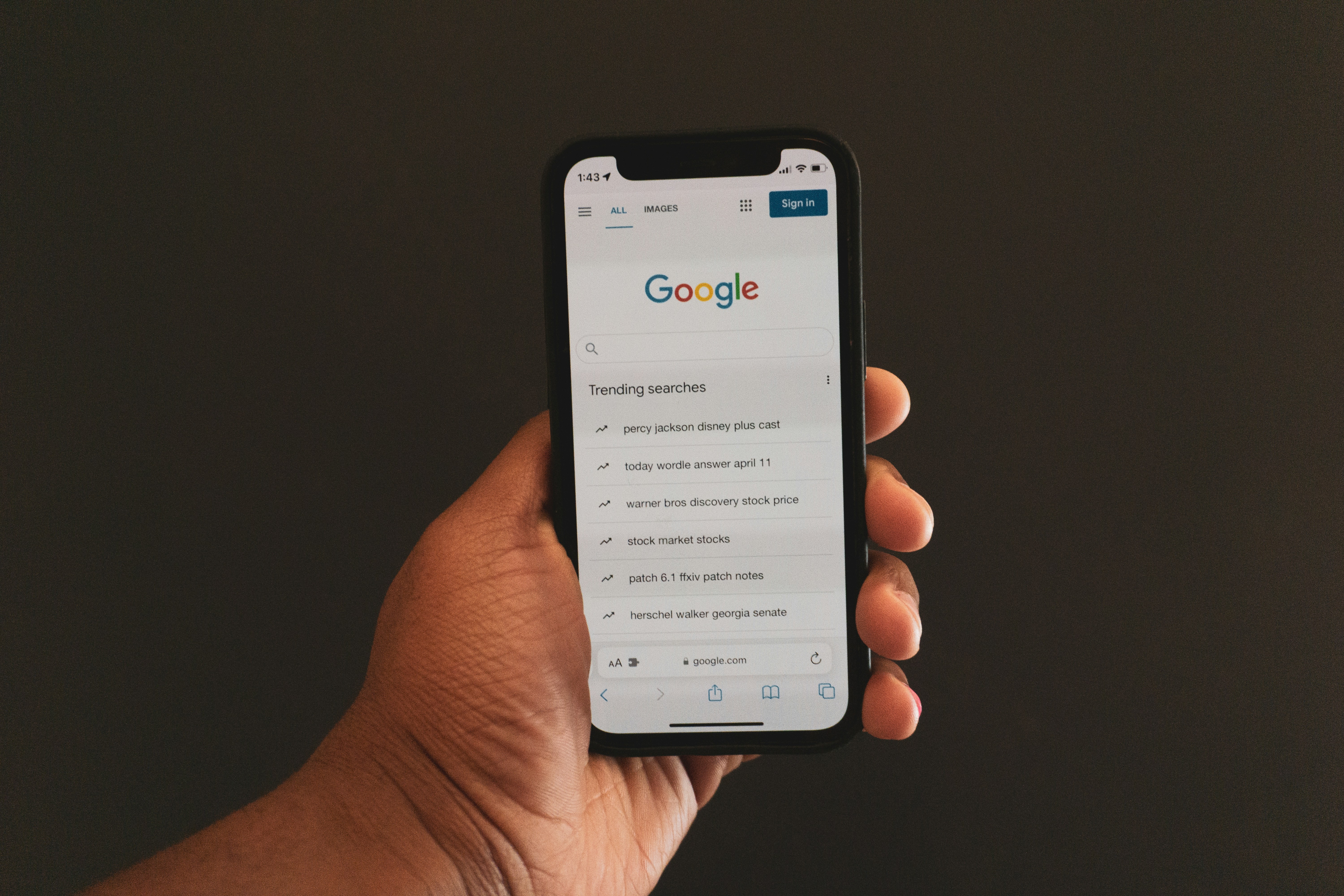 A hand holding a smartphone displaying the Google homepage with trending searches.